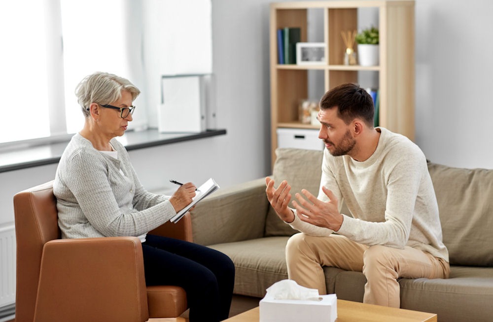 man sitting on couch for individual therapy while therapist takes notes