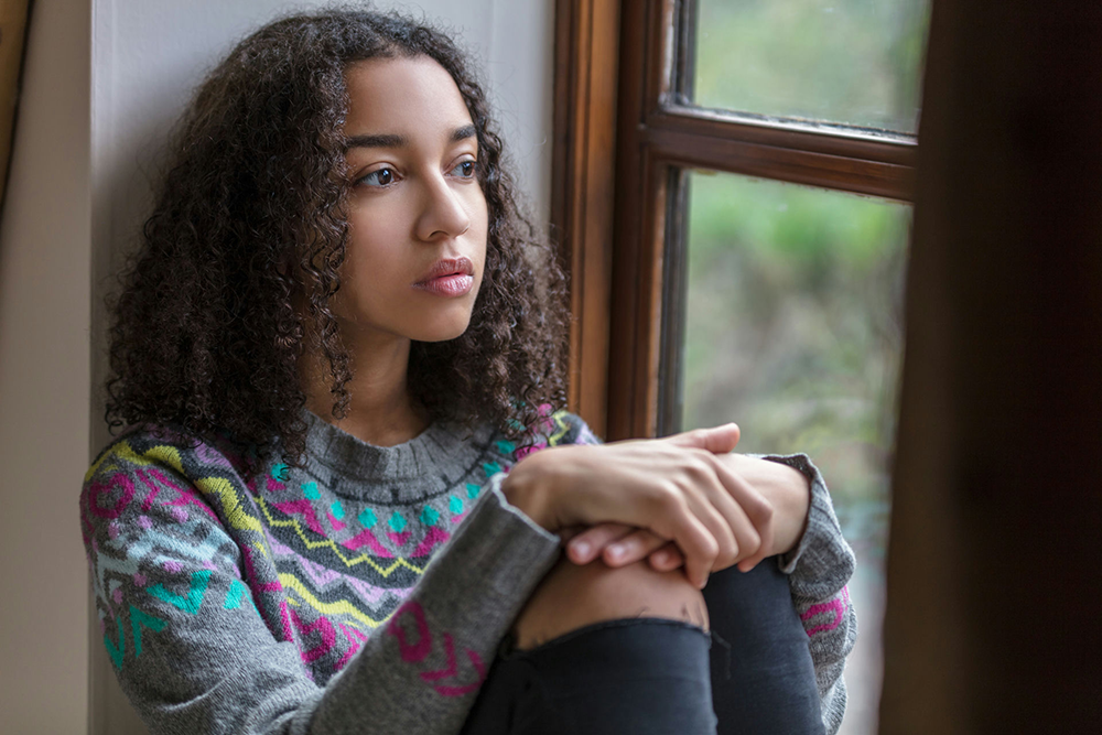 Teenager sitting alone looking out a window, symbolizing early warning signs of addiction in families.